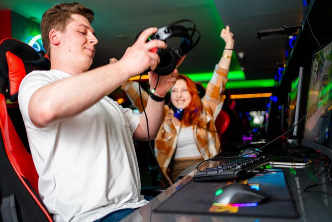 Um homem colocando o headset e uma mulher ao lado comemorando uma conquista em um game
