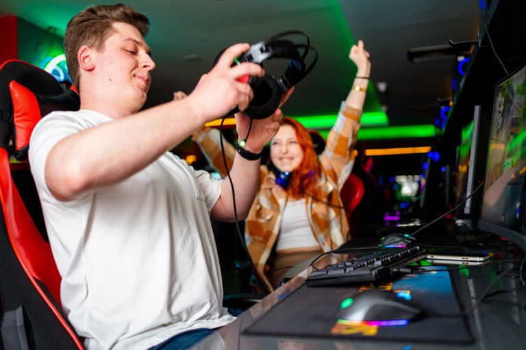 Um homem colocando o headset e uma mulher ao lado comemorando uma conquista em um game