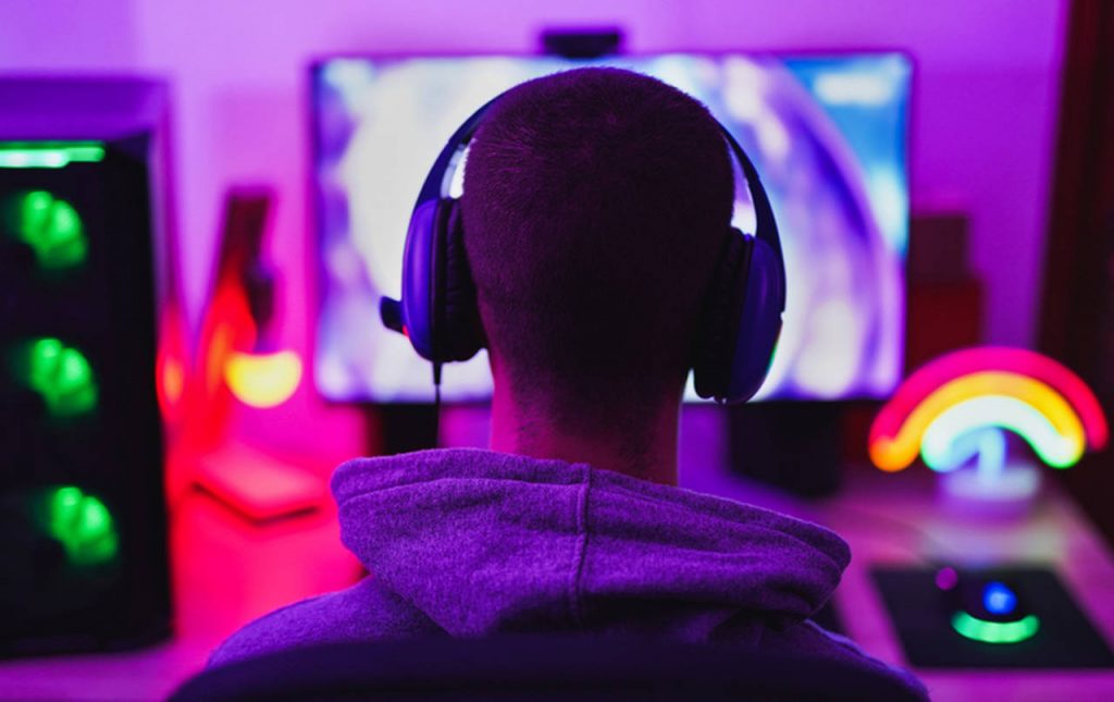 Pessoa de costas com um headset gamer olhando para um monitor enquanto transmite jogos na Twitch